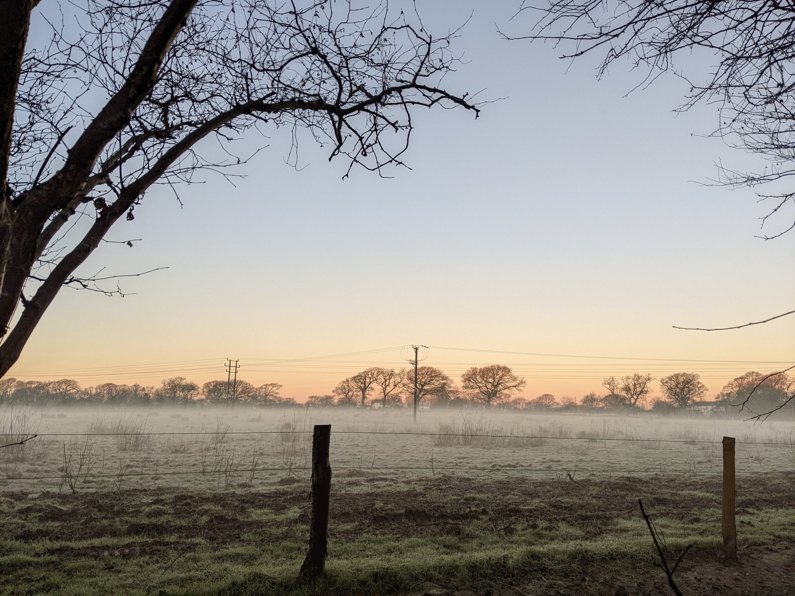 Sunrise over a misty field with fence in foreground