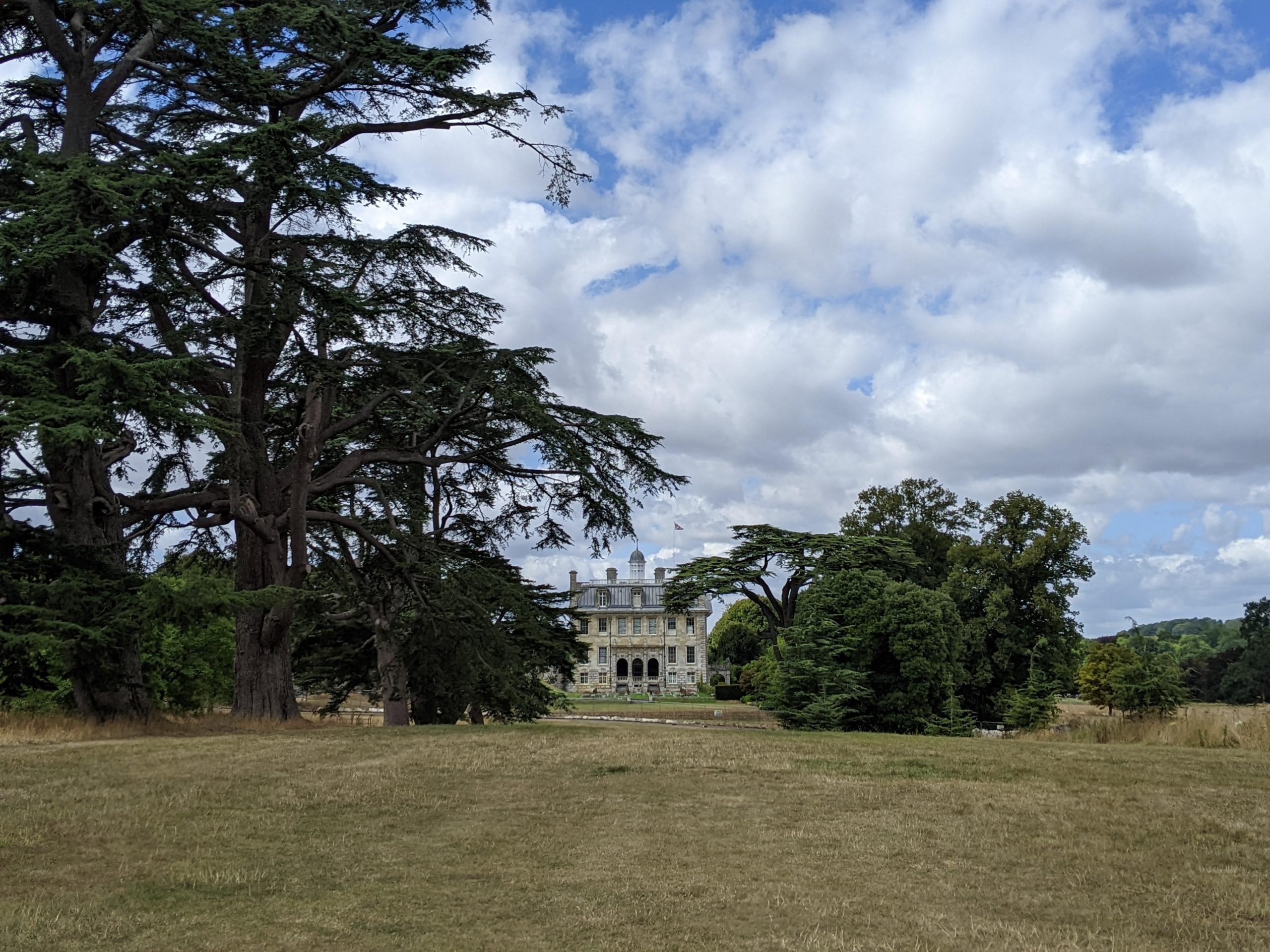 A stately home at the bottom of a long lawn bordered by trees